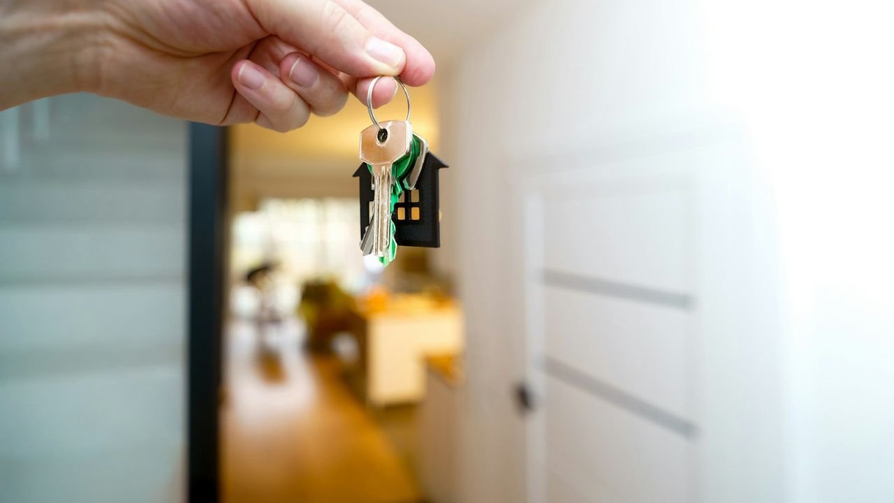 Hand holding house keys in front of an entrance