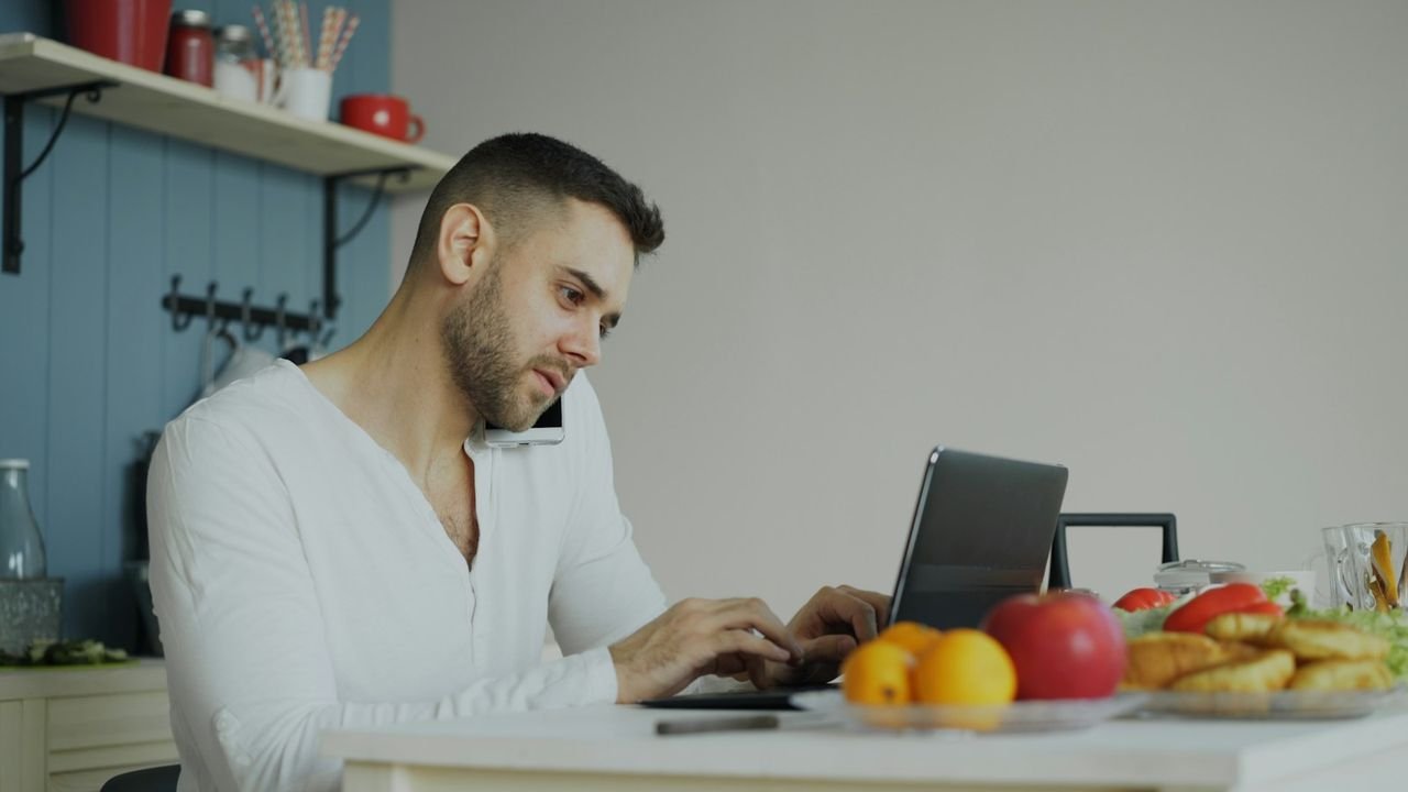 Business owner on the phone and laptop at a kitchen table, handling feedback